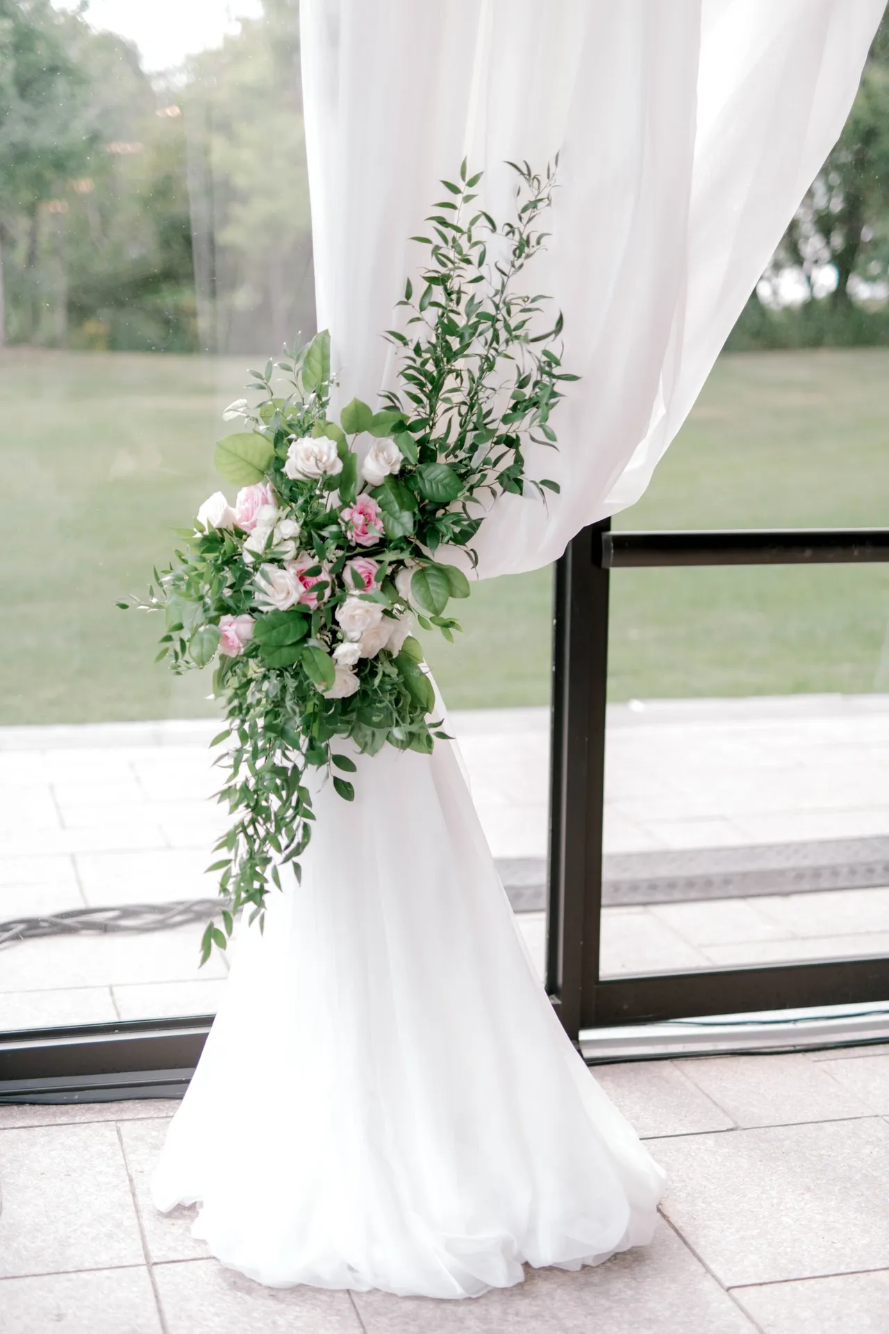 White ceremony drape tied with a cascading arrangement of pink and ivory roses and greenery