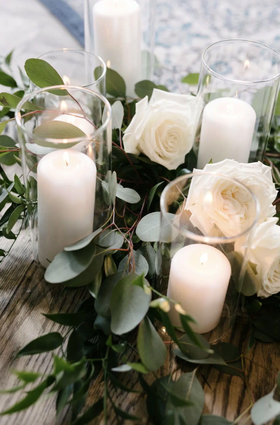 White pillar candles in glass cylinders among eucalyptus and white roses at Storys Building