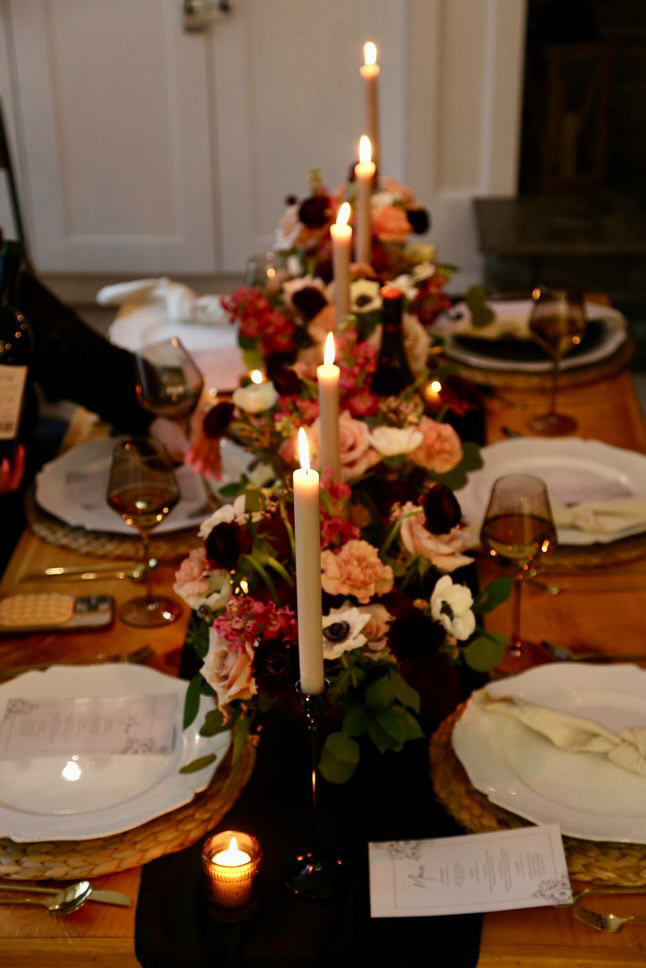 Candlelit table runner of roses, anemones and burgundy blooms with taper candles