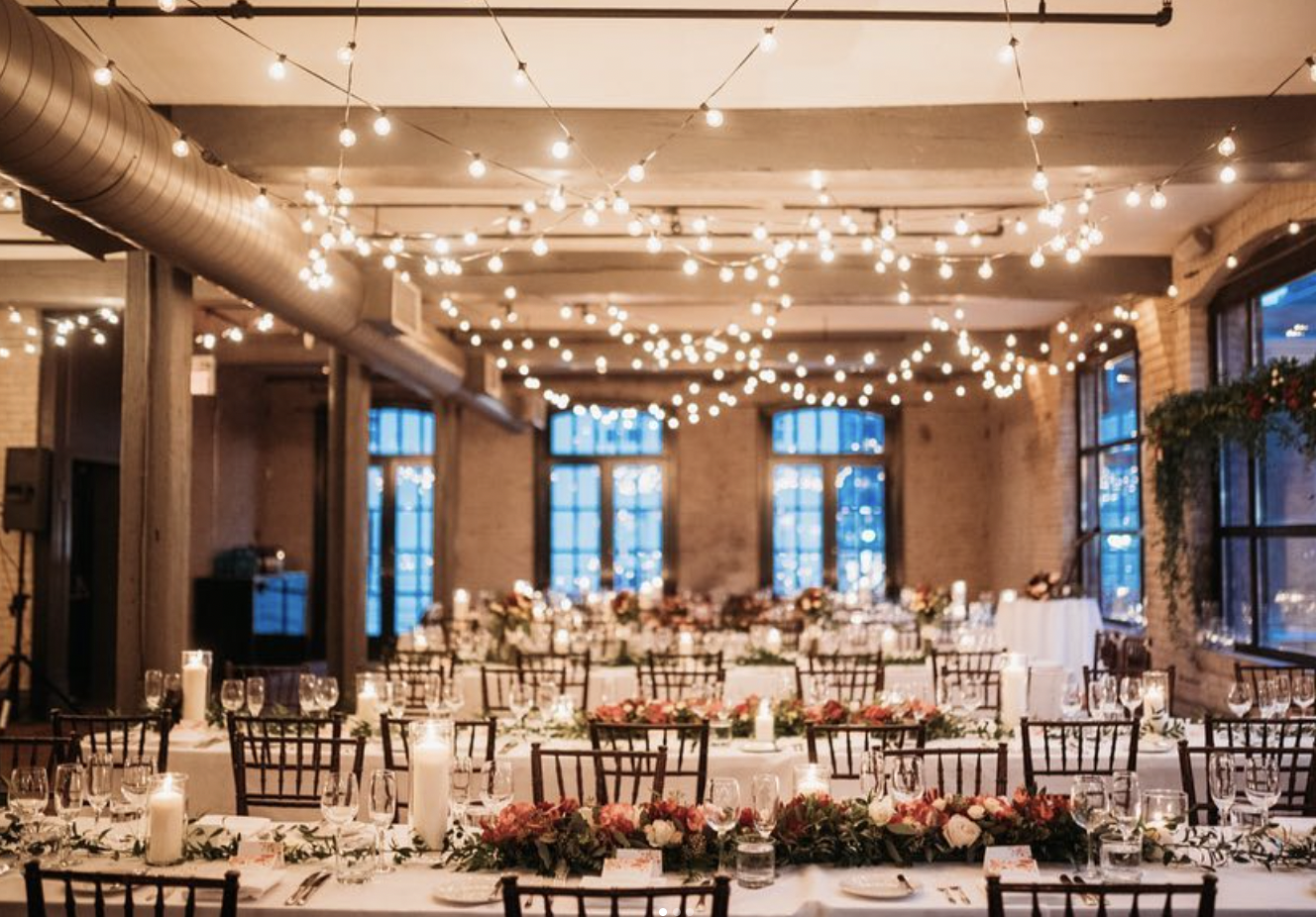 Storys Building reception with string lights, long tables, candles and red and ivory floral runners