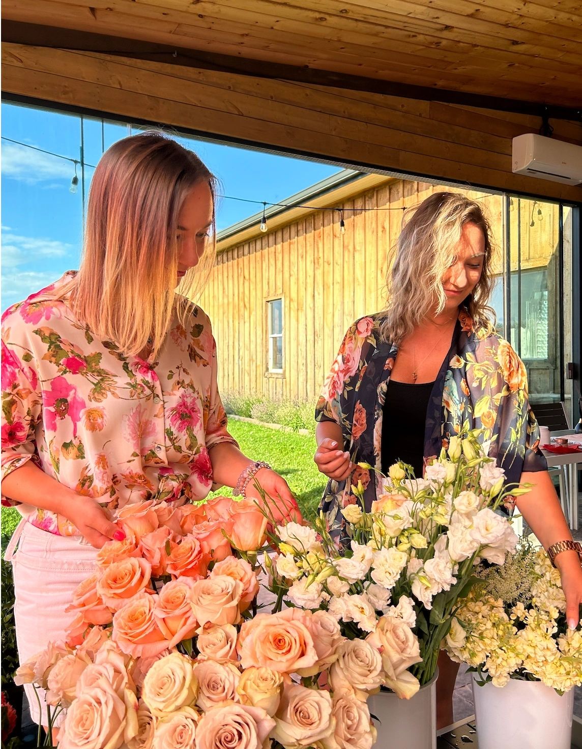 Kat and Vik with buckets of peach roses and white blooms at an outdoor workshop