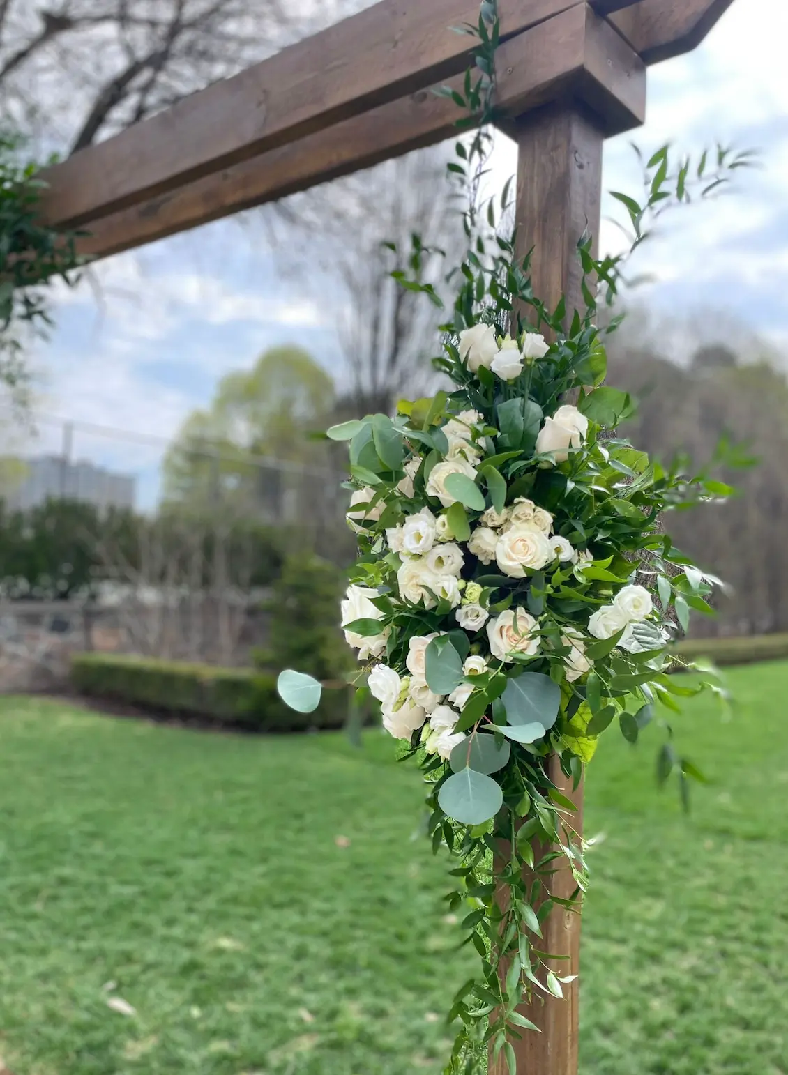Ivory roses, eucalyptus and trailing greenery on a wooden ceremony pergola in the garden at Graydon Hall Manor