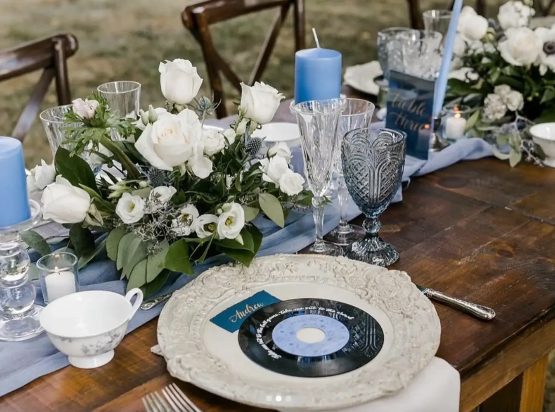 Place setting with a vinyl record name card, blue glassware and a white rose and lisianthus centrepiece