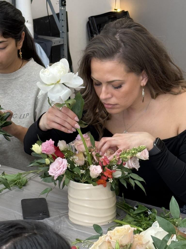 A guest placing a white peony into her arrangement of pink roses and snapdragons