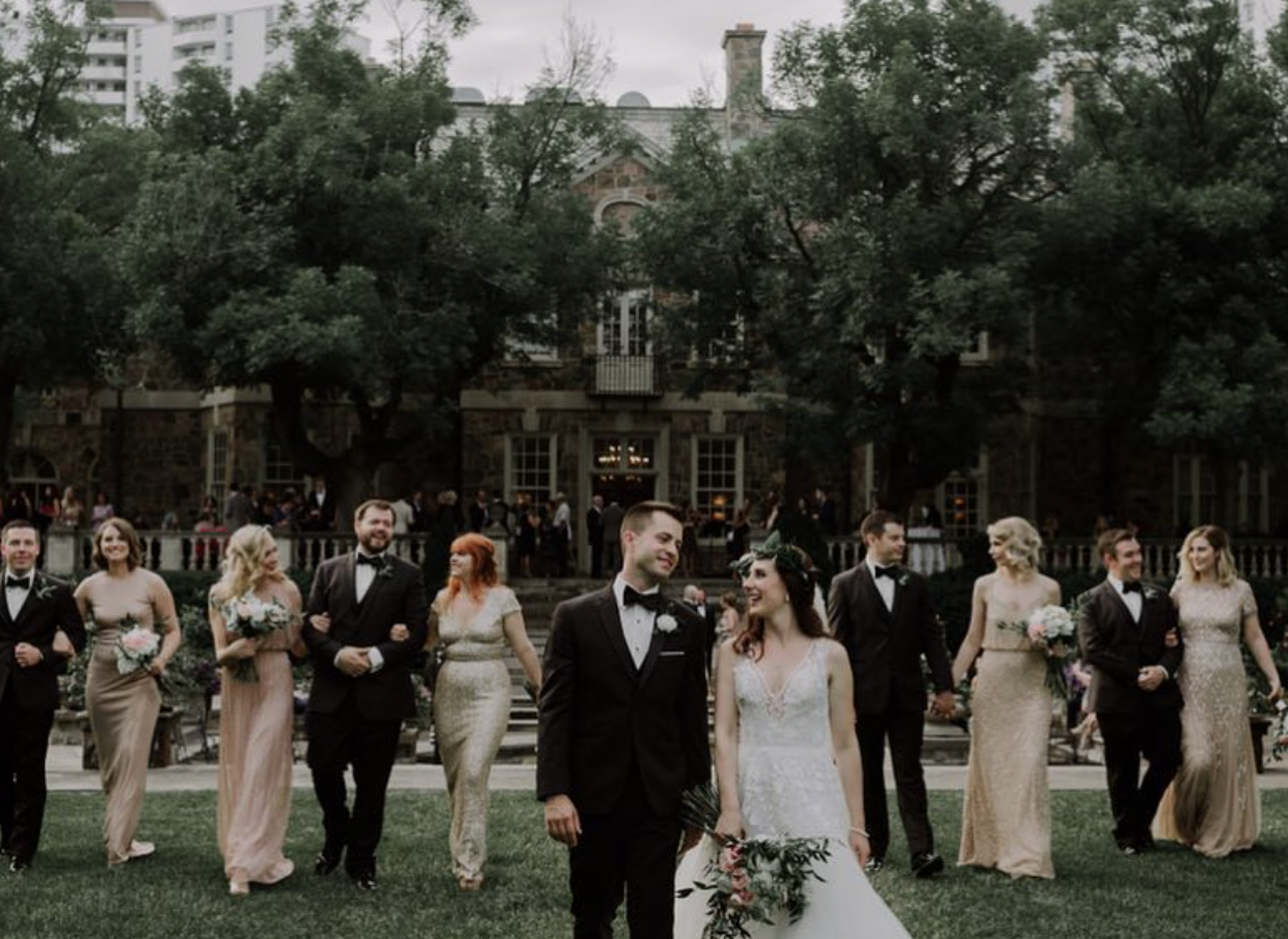 Newlyweds and their wedding party walking on the lawn in front of Graydon Hall Manor with blush bouquets