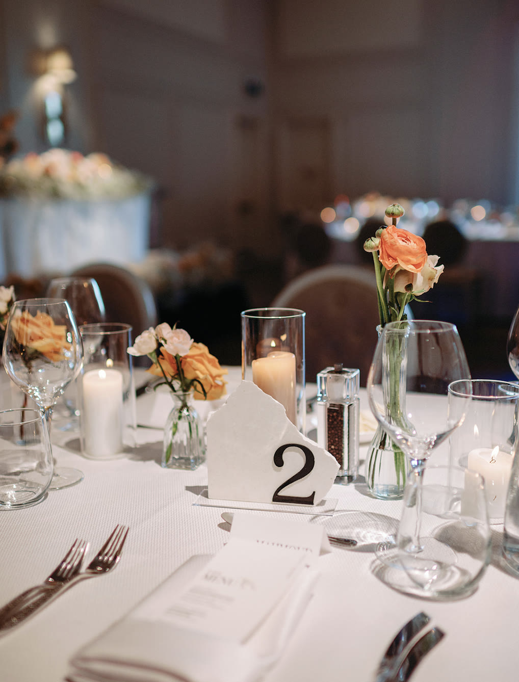 Table two with bud vases of peach ranunculus and roses beside candlelight at Arlington Estate