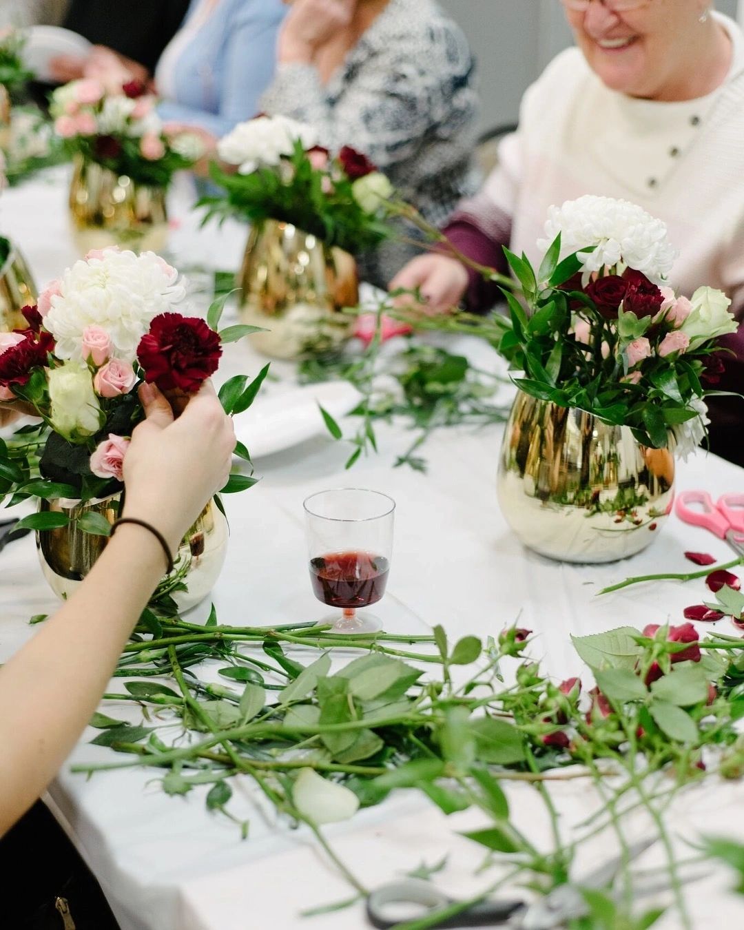 Guests arranging burgundy and white roses with wine and greenery on the table