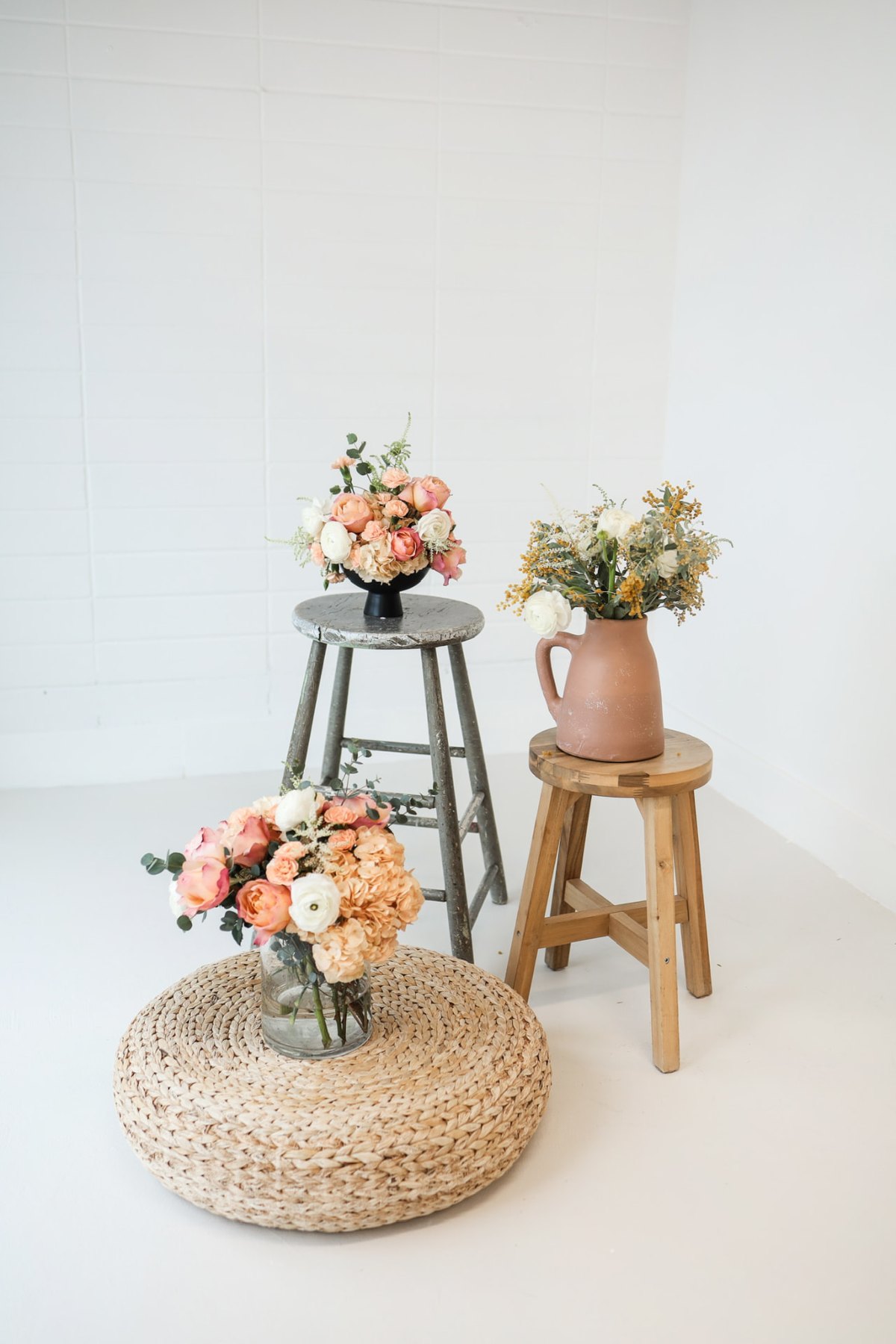 Blush and peach floral arrangements styled on wooden stools in a bright studio