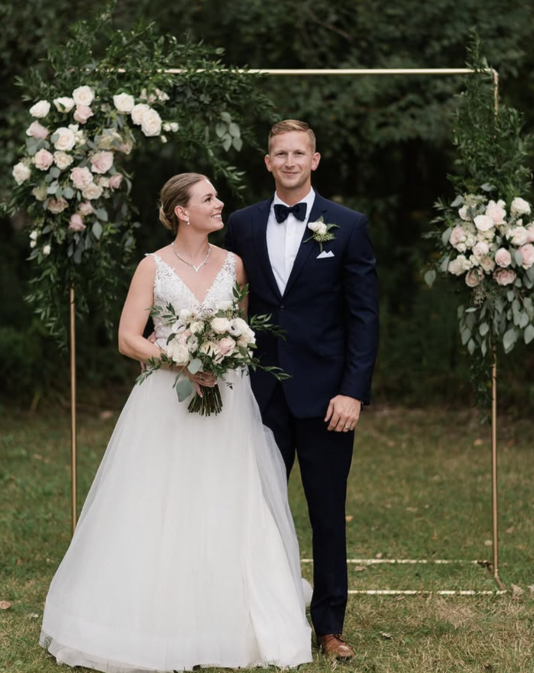 Couple beneath a gold arch dressed with blush roses and greenery