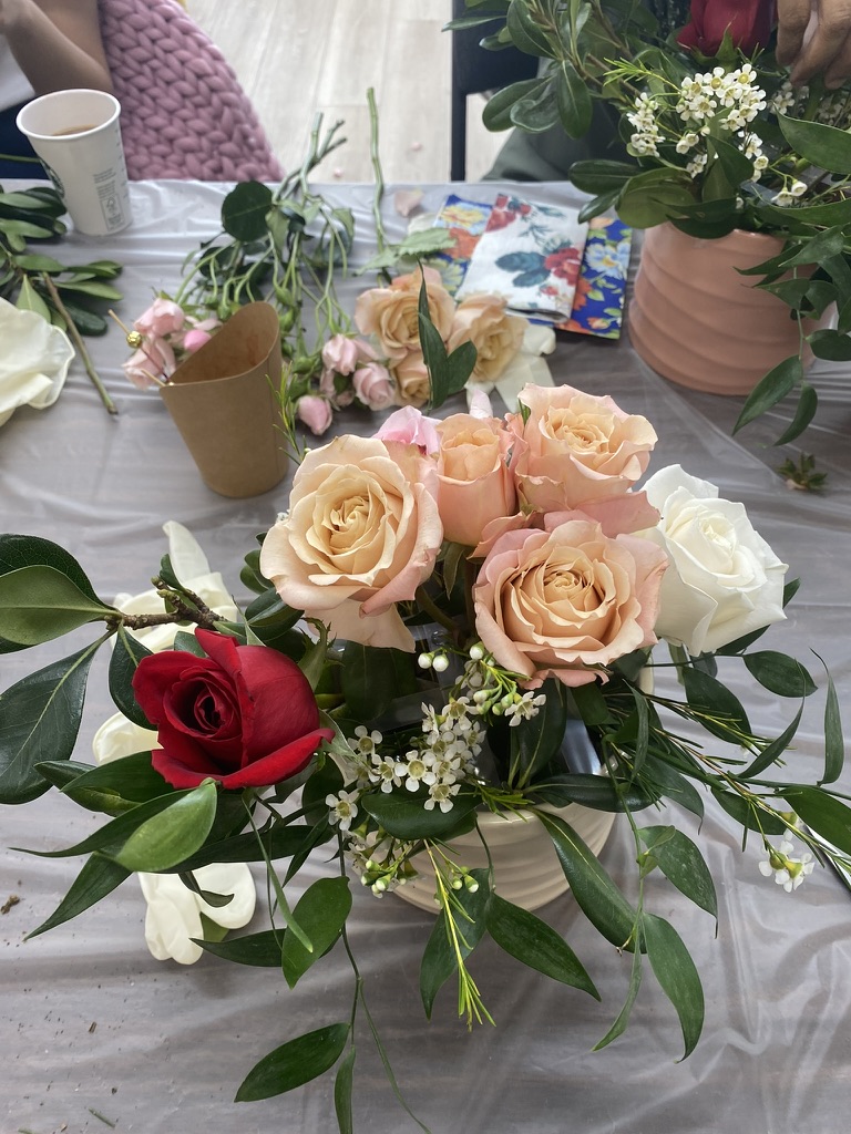 A finished arrangement of peach roses, a red rose and waxflower in a cream pot