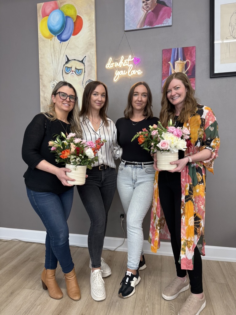 Four smiling workshop guests holding their finished arrangements in cream pots