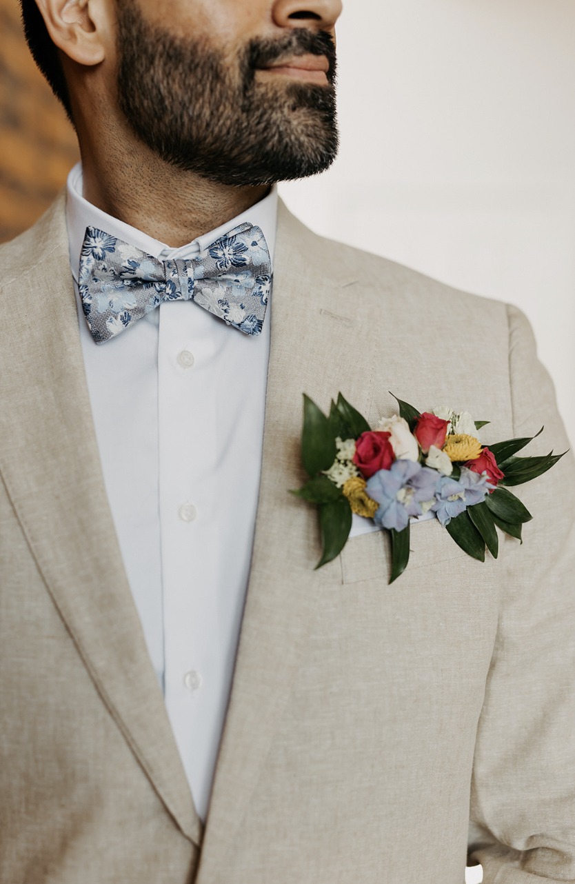 Kaustav’s colourful boutonniere on his linen suit beside a floral bow tie