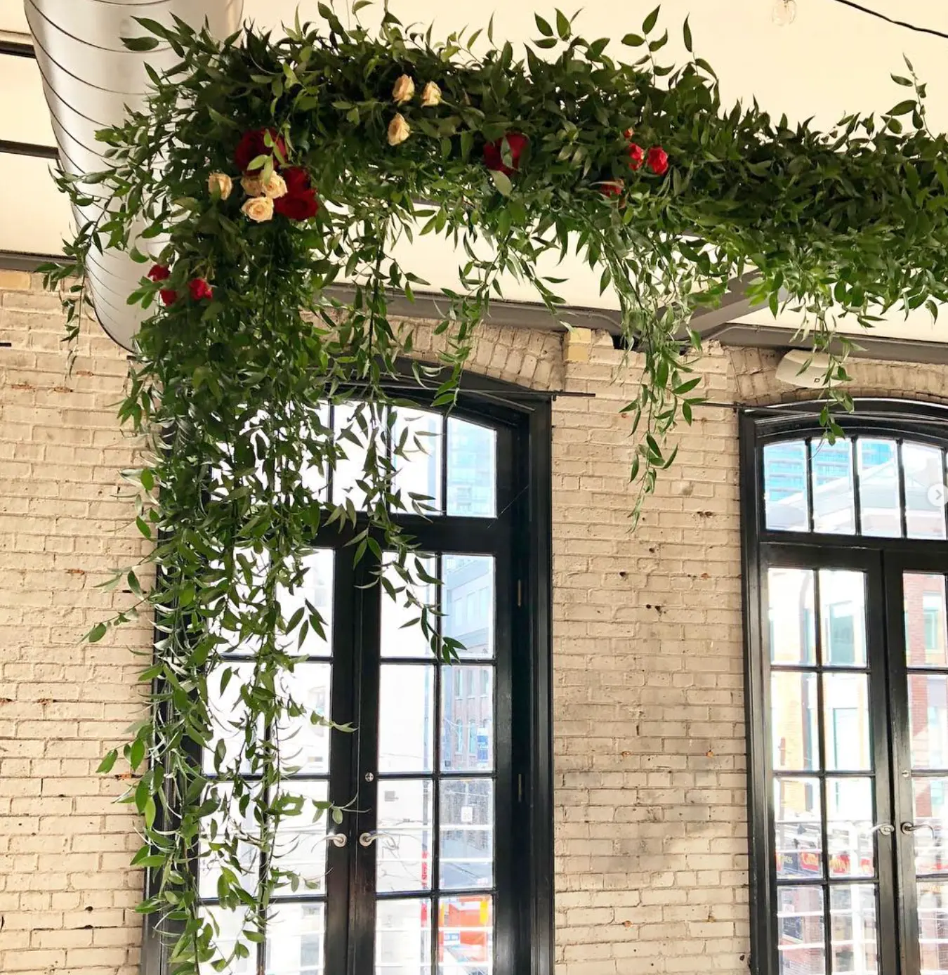 Hanging greenery installation with red and peach roses over the brick-walled windows