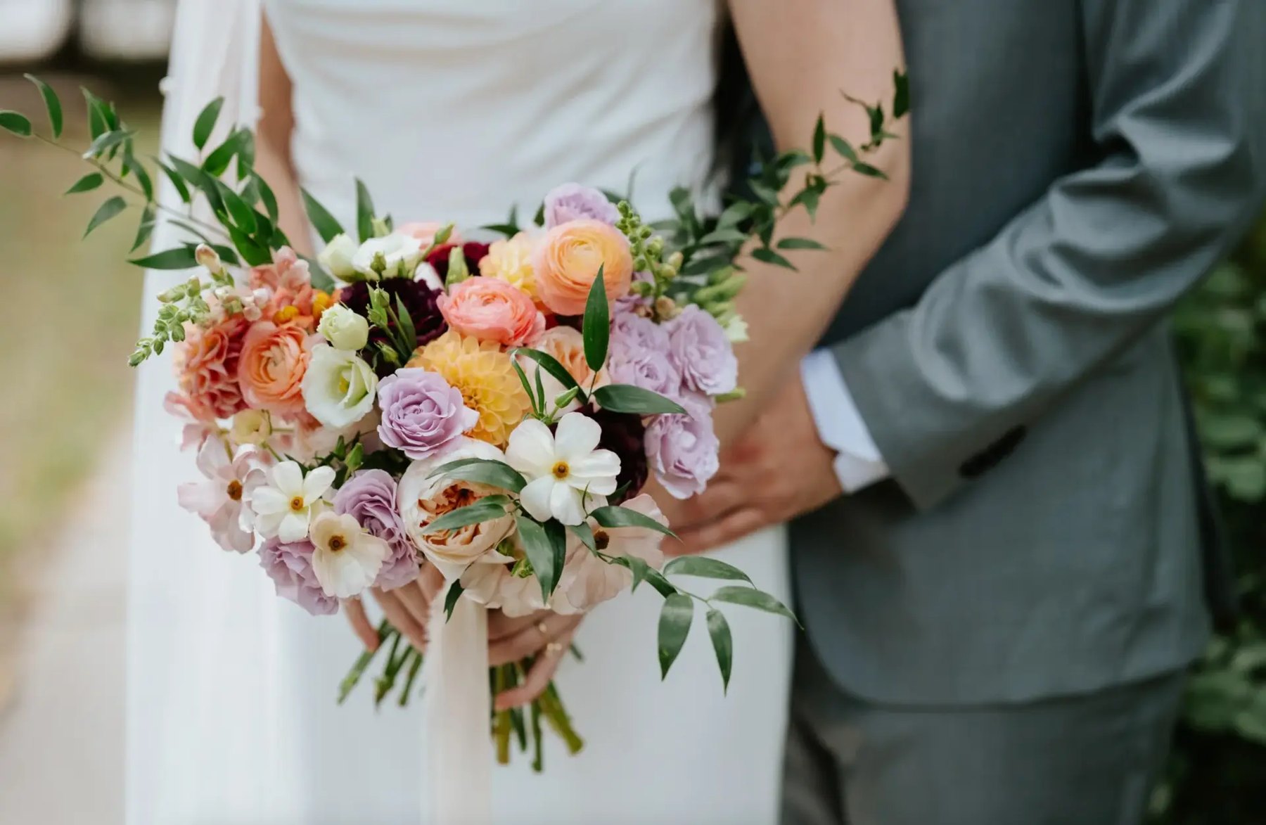 Bride and groom holding a colourful garden bouquet of roses, ranunculus, and lisianthus