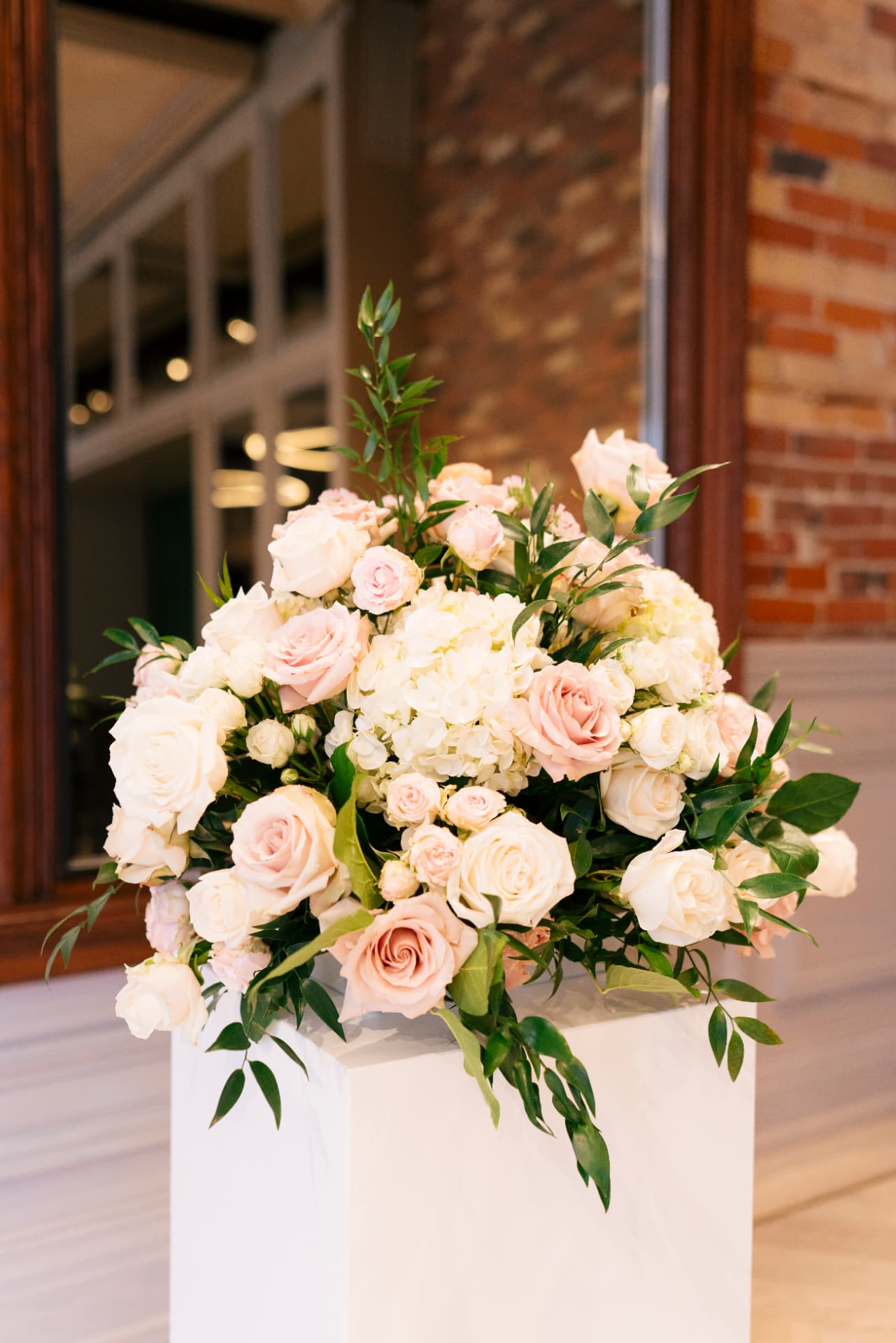 Blush and ivory roses with greenery arranged on a pedestal at Hannah and Kyle’s wedding