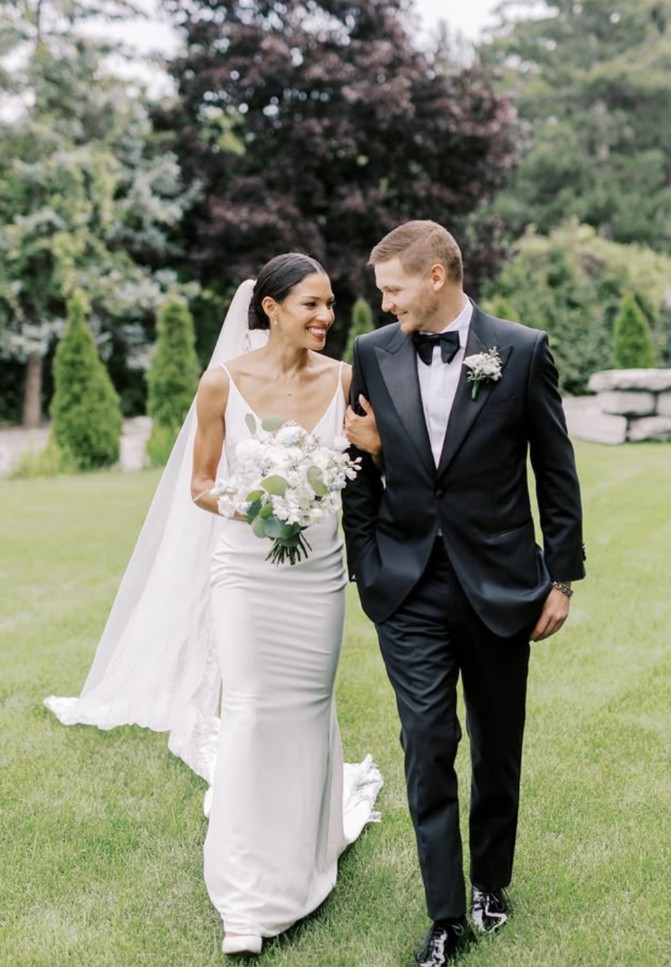 Bride and groom walking arm in arm across a lawn with a white and pale blue bouquet