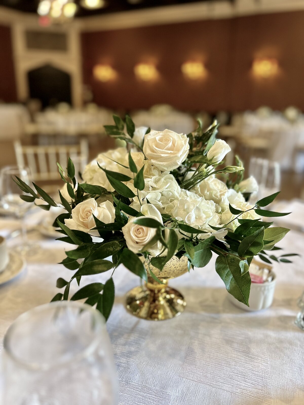 Ivory rose and hydrangea centrepiece with greenery in a gold vessel