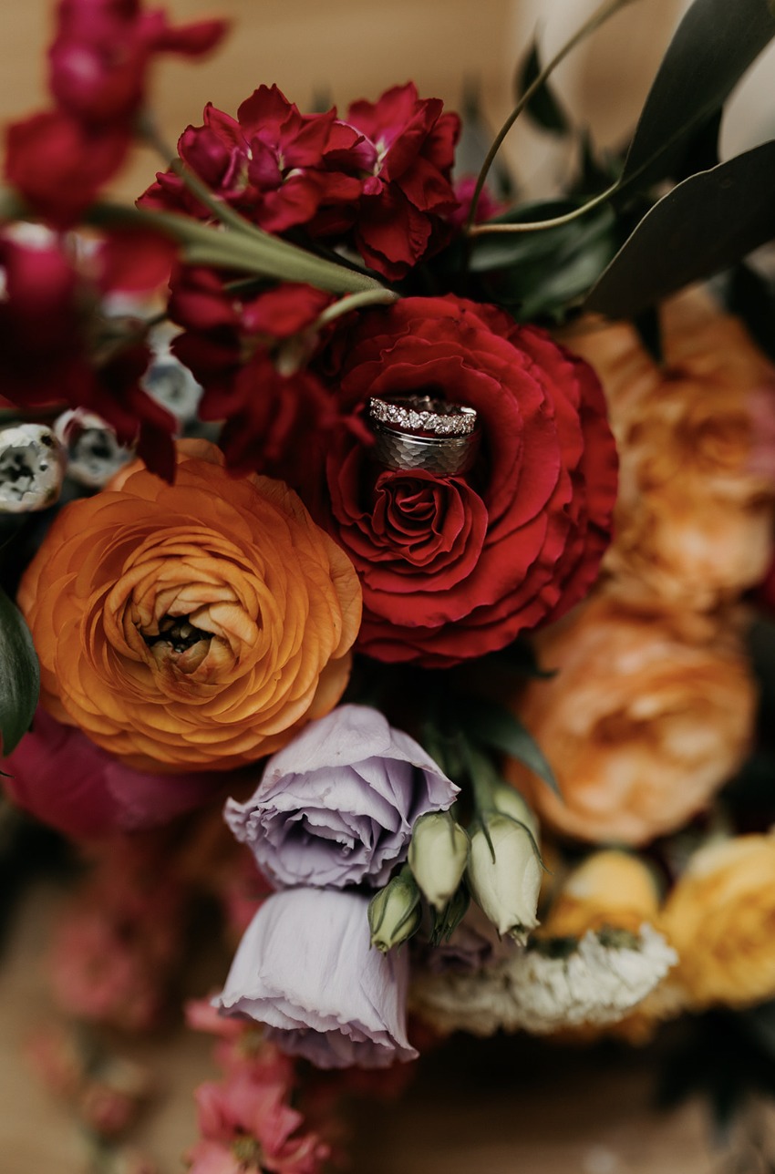 Wedding rings nestled in a red rose among Lydia and Kaustav’s wedding flowers