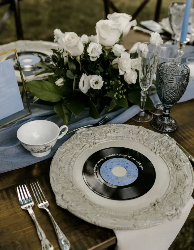 Ornate charger with a vinyl record, vintage teacup and white rose arrangement on a dusty blue runner