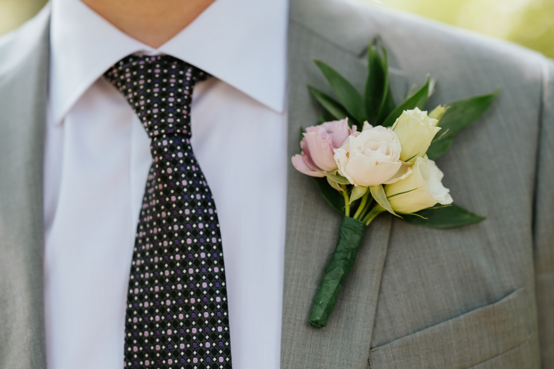 Liam’s boutonnière of lilac and ivory spray roses with ruscus on a grey suit
