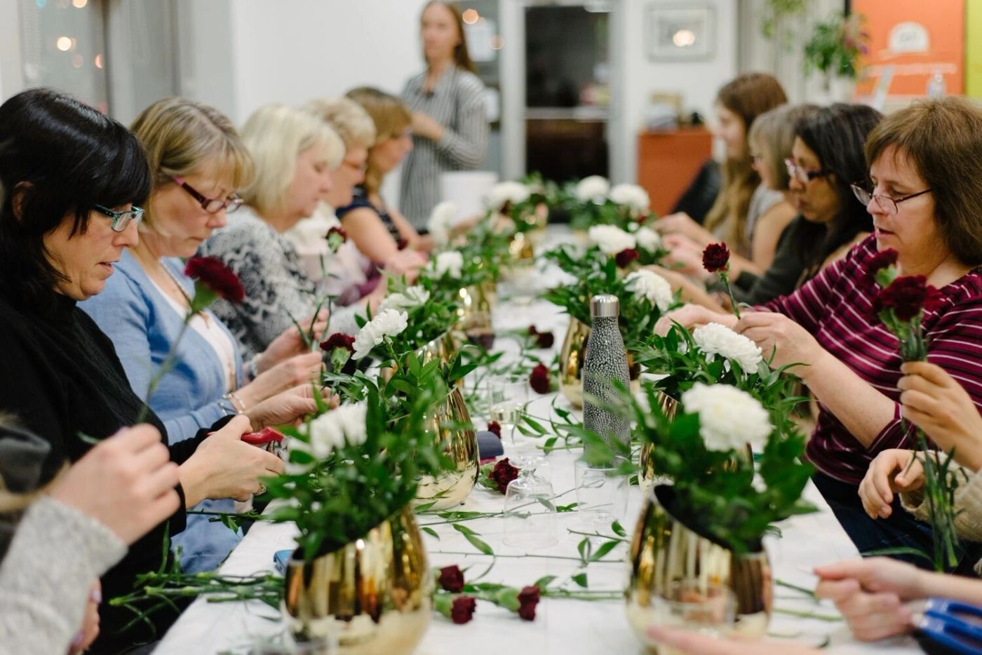 Guests at a long table arranging white roses and greenery in gold vases