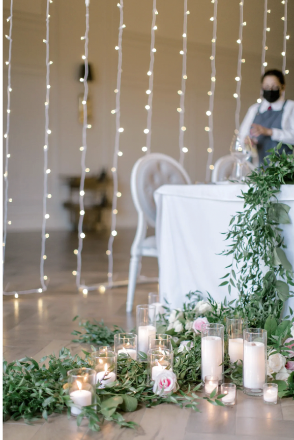 Head table at Arlington Estate with trailing greenery, roses and pillar candles beneath string lights