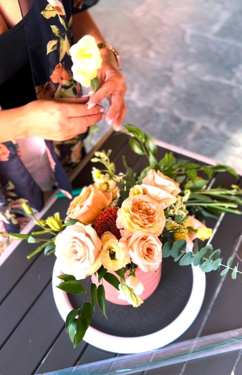 A guest finishing an arrangement of peach garden roses in a pink pot