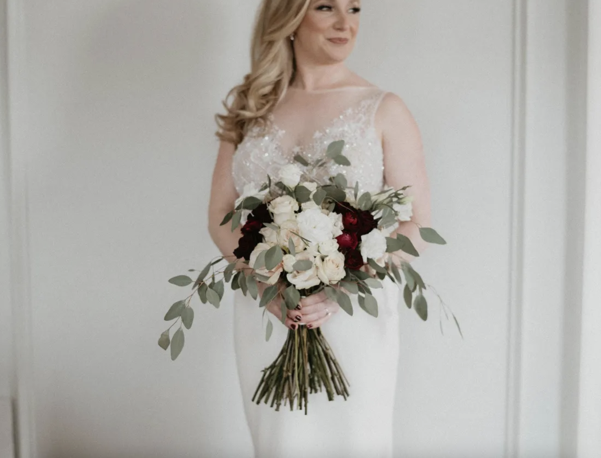 Jessica holding her bouquet of ivory roses, burgundy ranunculus and trailing eucalyptus